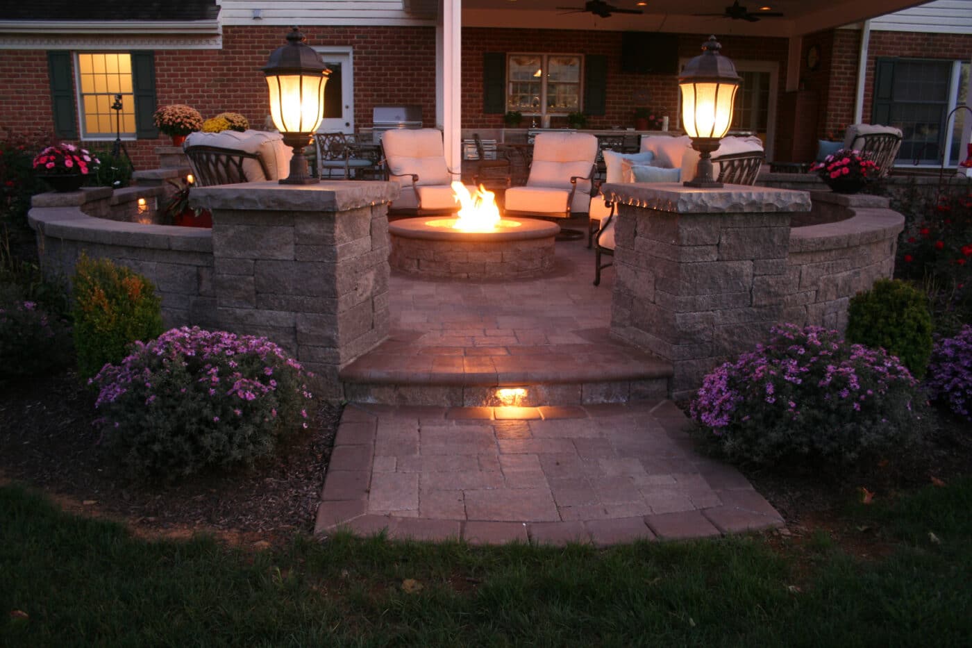 back patio with circular retaining wall around it featuring chairs around a fireplace