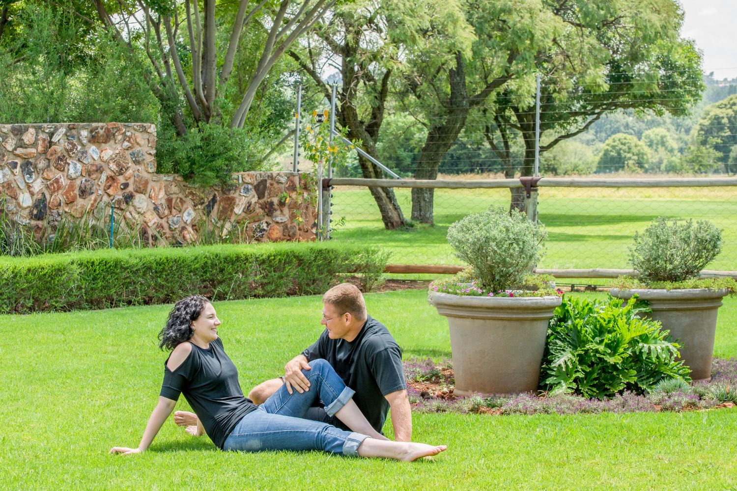 Happy couple in green grassy backyard with stone wall, gate and trees - free of silica in home environment
